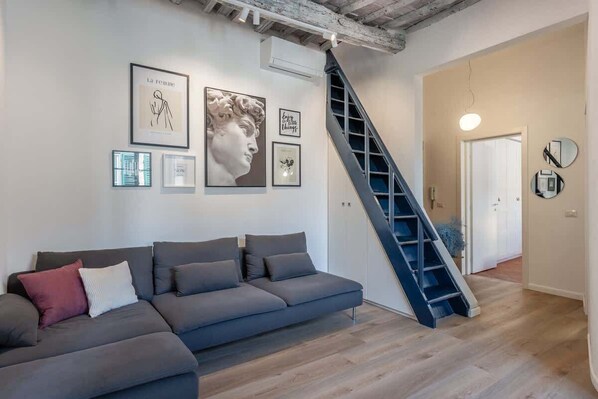 A modern living room with a grey sectional sofa, a staircase, and artwork on the walls.