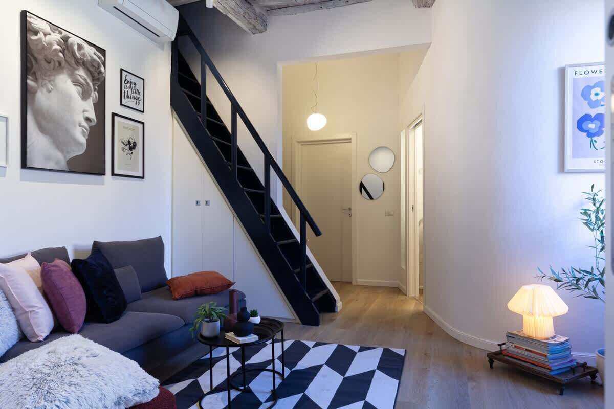 A modern living room with a grey sofa, a black staircase, and a black and white rug.