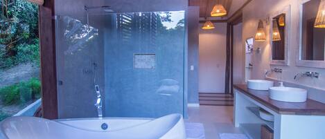 A modern bathroom with a large bathtub, two sinks, and a glass-enclosed shower.