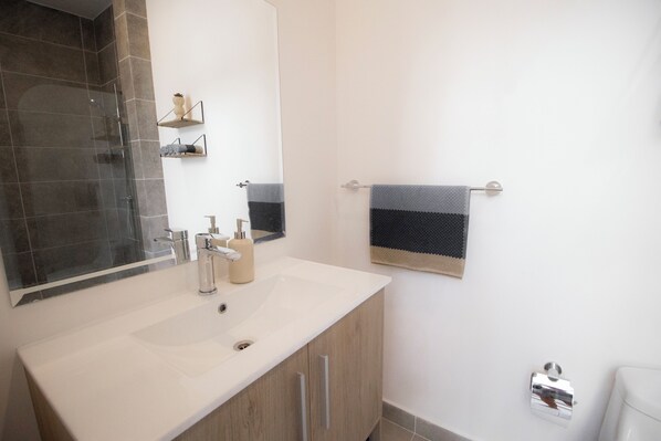 Et badeværelse med en hvid vask, glasvæg til brusebad, et håndklædestativ med et stribet håndklæde og en toiletpapirholder.