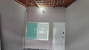 Una habitación con piso de baldosas, una ventana con celosía verde y una puerta blanca.