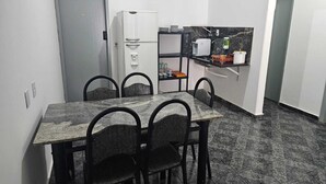 Una cocina compacta con una mesa de comedor y cuatro sillas, un refrigerador, una cafetera y un estante pequeño con utensilios de cocina.