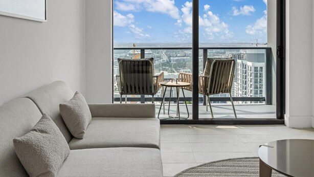 Ein modernes Wohnzimmer mit einer Couch, einem Couchtisch und Blick auf die Stadt durch große Fenster.
