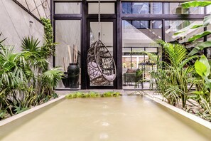 A serene indoor garden with a hanging chair, potted plants, and a calm water feature. - ANANA Casa Karmond (Tulum)