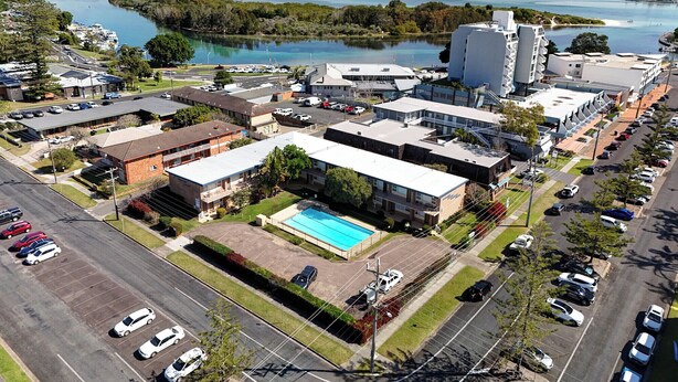 An aerial view of a commercial area with a large building featuring a swimming pool, surrounded by parking lots and roads. - Forster Lodge 16: 1  BR, 1  BA Apartment in Forster, Sleeps 4 (Forster)