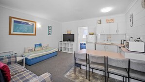 A compact living space with a kitchenette, a sofa with beach-themed cushions, a television, and a framed picture of a beach scene. - Forster Lodge 16: 1  BR, 1  BA Apartment in Forster, Sleeps 4 (Forster)