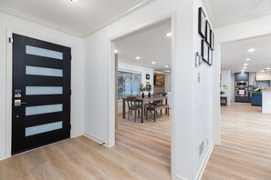 A modern interior with a black door, wooden flooring, a dining area with a table and chairs, and a kitchen in the background. - Centrally located cozy home close to everything. (San Antonio)