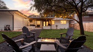 A backyard with a fire pit, four Adirondack chairs, and a house with string lights.