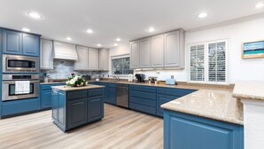 A modern kitchen with blue cabinets, stainless steel appliances, and a granite countertop.