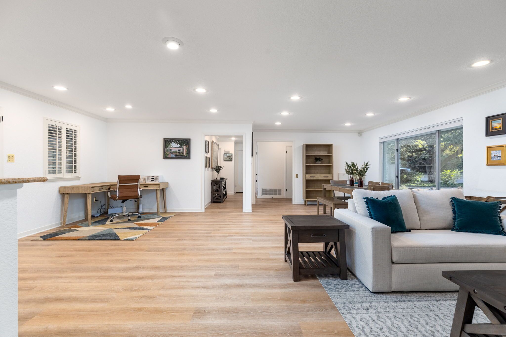 A spacious living area with a wooden floor, a sofa, a dining table, and a kitchen area in the background.