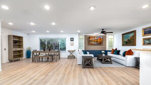 A spacious living area with a wooden floor, a white sofa, a dining table with chairs, and a ceiling fan.