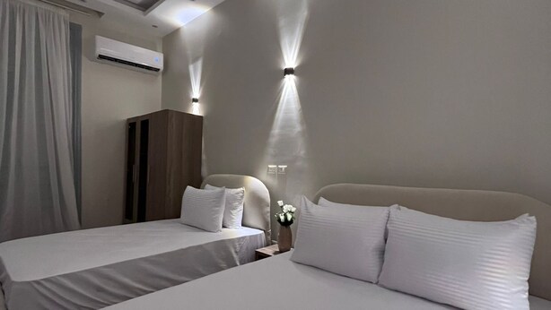 Une chambre d’hôtel avec deux lits, une armoire, un appareil de climatisation et des lampes fixées au mur.