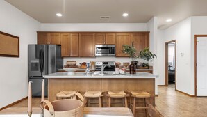 A modern kitchen with wooden cabinets, stainless steel appliances, and a central island with bar stools. - 3 bedroom, 2 bath with fire pit and game room (Kennewick)
