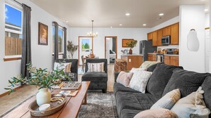 A spacious living room with a dark grey sofa, a wooden coffee table, and a large window with curtains. - 3 bedroom, 2 bath with fire pit and game room (Kennewick)