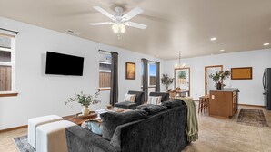 A spacious living room with a large gray sofa, a flat-screen TV mounted on the wall, and a ceiling fan. - 3 bedroom, 2 bath with fire pit and game room (Kennewick)