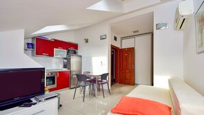A compact hotel room with a kitchenette, a dining area, and a bed with an orange pillow.