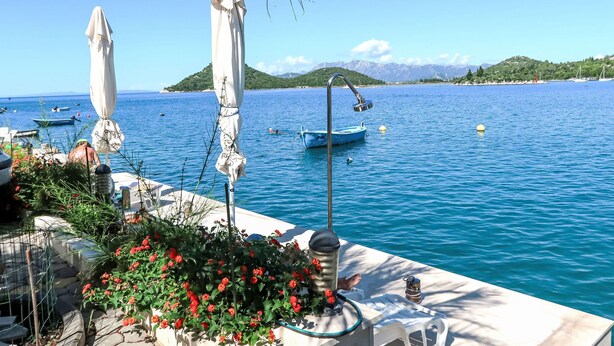 A seaside patio with umbrellas, a boat, and a mountainous backdrop.