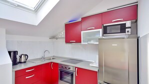 A compact kitchen with red cabinets, a stainless steel refrigerator, a microwave, and a gas stove.