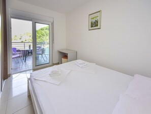A hotel room with a bed, a small desk, a chair, and a balcony with outdoor seating.