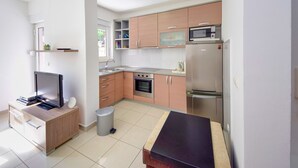 A compact kitchen with a microwave, oven, and refrigerator. There is a small trash bin and a wooden cabinet. - Jasmina by Interhome (Blace)