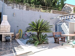 A patio with a grill, a bicycle, a palm tree, and a shed.