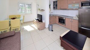 A modern kitchen with wooden cabinets, a stainless steel refrigerator, and a built-in oven. There is a dining area with a glass table and yellow chairs. - Jasmina by Interhome (Blace)