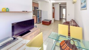 A modern living room with a flat-screen TV, glass dining table, yellow chairs, a sofa, and a kitchen in the background. - Jasmina by Interhome (Blace)