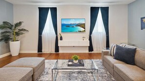 A living room with a sofa, coffee table, and a large window with curtains. - Heart of Cocoa Beach, Rooftop Deck, Hammock & Private Balcony (Cocoa Beach)