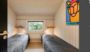 Quarto com duas camas, uma janela, paredes de madeira e um pôster na parede.