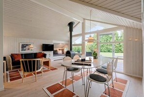 Uma sala de estar moderna com sofá, mesa de jantar, cadeiras, lareira e grandes janelas.