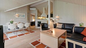 Et moderne interiør med spiseplads, en stue med sofa og sofabord, og et køkken i baggrunden.