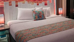 Ein Hotelzimmer mit einem großen Bett, einem weißen Kopfteil und einem farbenfrohen, abstrakten Wandbild.