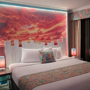 Une chambre d’hôtel avec un grand lit, une tête de lit blanche et une fresque murale abstraite aux couleurs vives.