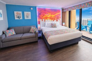 A hotel room with a bed, a sofa, artwork on the walls, and a view of the outside.