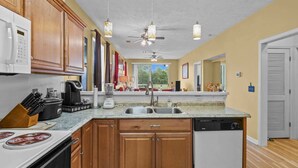 A kitchen with wooden cabinets, a microwave, a stove, a dishwasher, and pendant lights. - River Oaks 48-D (Myrtle Beach)