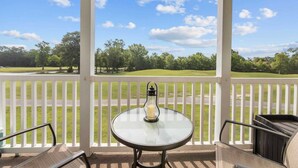 A covered outdoor area with a table and chairs, a white railing, and a view of a golf course. - River Oaks 48-D (Myrtle Beach)