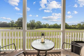 A covered outdoor area with a table and chairs, a white railing, and a view of a golf course. - River Oaks 48-D (Myrtle Beach)