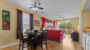 A dining area with a table and chairs, a red sofa, ceiling fans, and a large window with curtains. - River Oaks 48-D (Myrtle Beach)