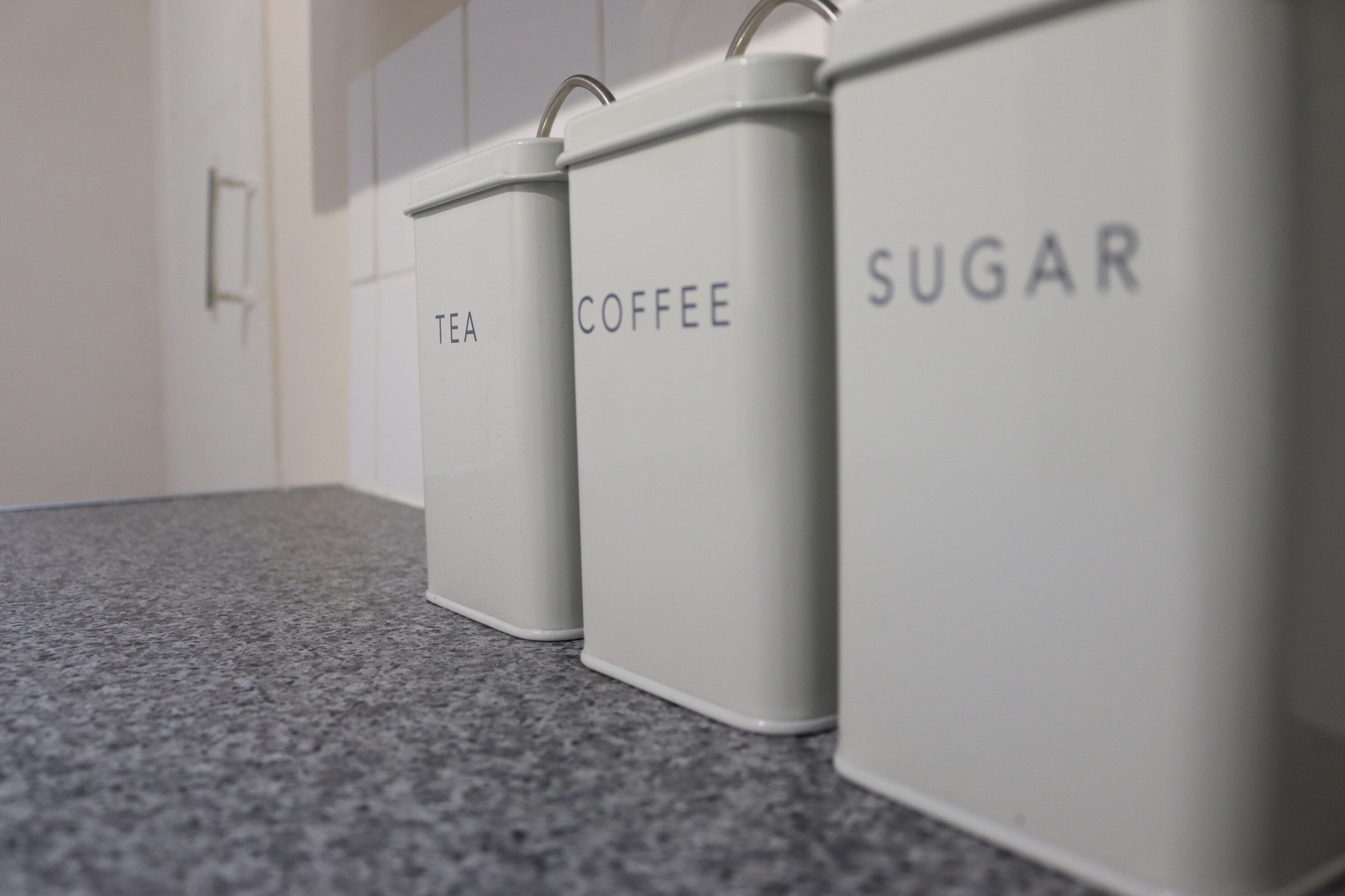 Three white containers labeled tea, coffee, and sugar on a kitchen counter.