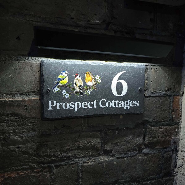 A house number sign for Prospect Cottages, featuring three birds and floral decorations.