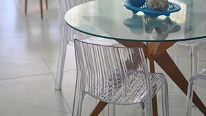 Una sala de estar moderna con una mesa de comedor de vidrio, sillas transparentes, un ventilador de techo y una lámpara decorativa.