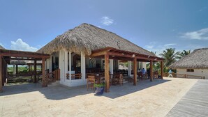 Un resort en la playa con estructuras de techo de paja, mobiliario exterior y una terraza de madera.