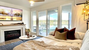Een slaapkamer met een groot bed, een open haard, een televisie en uitzicht op een meer.
