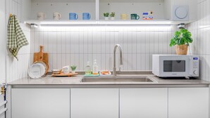 Una cocina moderna con armarios blancos, microondas integrado y una estantería con tazas variadas y un calendario.