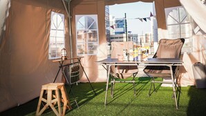 Un área con carpas, una mesa, sillas y un taburete. Se ven ventanas y luces colgantes.