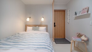 Un dormitorio con cama, lámparas de noche, una puerta de madera, una estantería con libros y una silla.