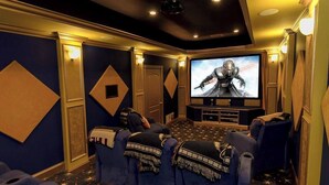 Un salón de cine en casa con una pantalla grande, asientos azules y una alfombra con diseños de estrellas.