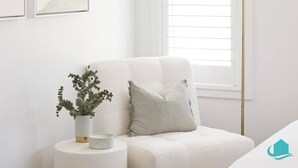 A white sofa with a striped pillow and a small potted plant on a white side table. - Moonee Retreat - 200m to beach and ocean reserve views (Catherine Hill Bay)
