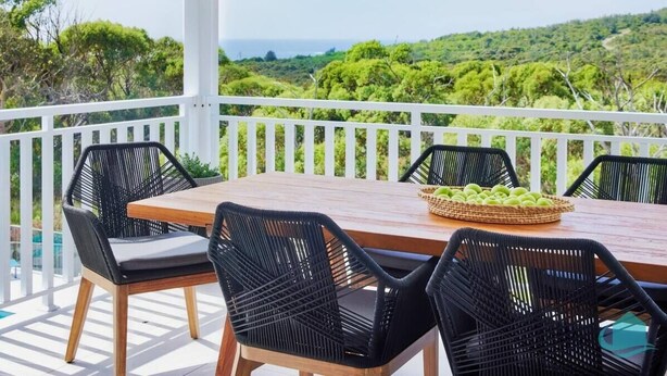 A wooden table with black wicker chairs on a balcony with a white railing, overlooking a lush green landscape. - Moonee Retreat - 200m to beach and ocean reserve views (Catherine Hill Bay)