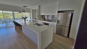 A modern kitchen with a central island, stainless steel appliances, and a view of the outdoors. - Moonee Retreat - 200m to beach and ocean reserve views (Catherine Hill Bay)